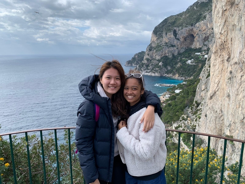 Two friends embrace at a cliff-top lookout with Capri’s dramatic coastline below