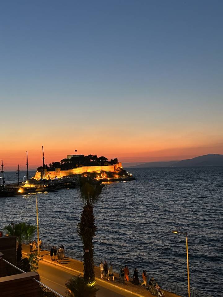 Vue en bord de mer au coucher du soleil avec des bâtiments illuminés.