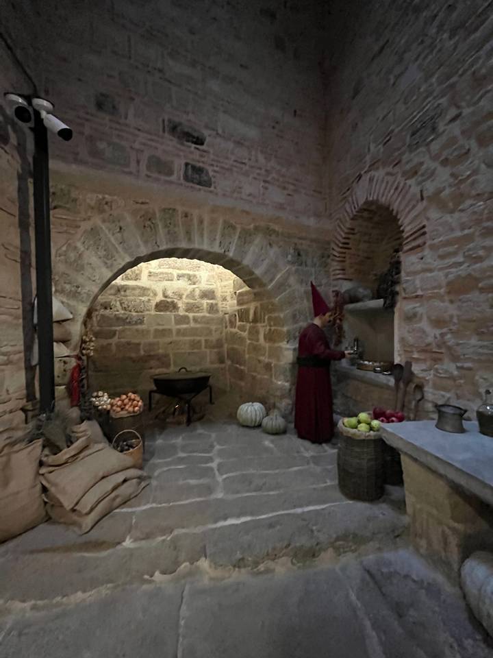 Pièce faiblement éclairée avec une silhouette en robe rouge et des murs en pierre.