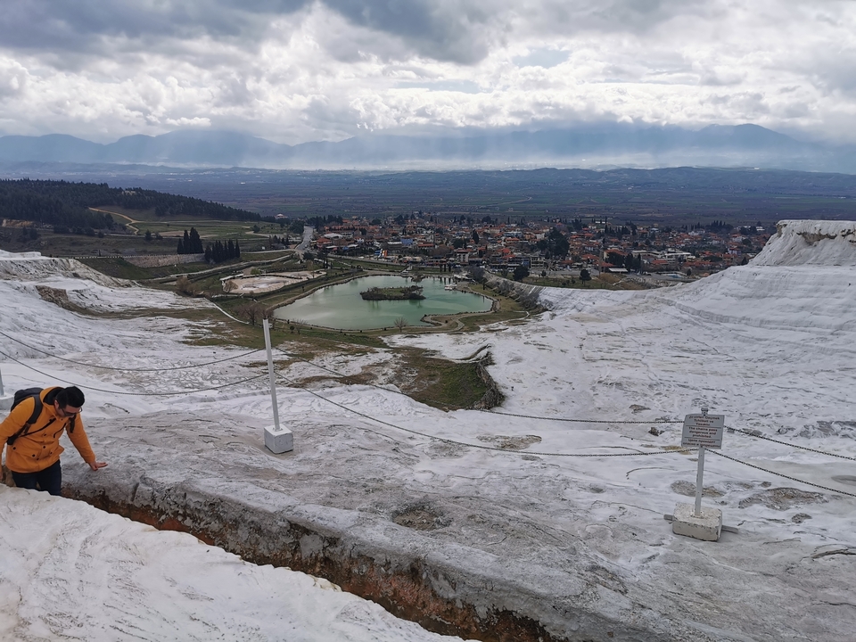 Vue panoramique de Pamukkale avec des terrasses enneigées et une ville en arrière-plan. Une personne en veste jaune est visible.