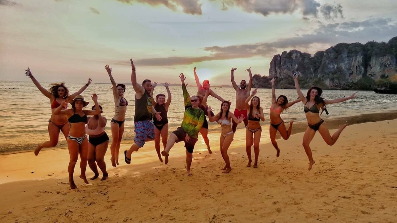 Group of people jumping in the air on a beach at sunset.