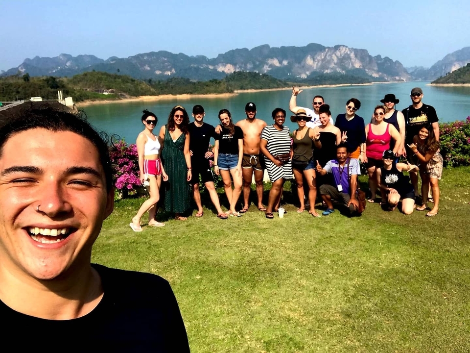 Group of people on a lawn with mountains and a lake in the background.