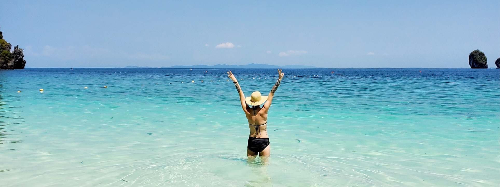 Person standing in shallow ocean water with arms raised.