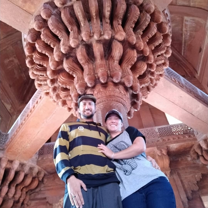 Couple se tenant debout sous une structure architecturale ornée avec des sculptures détaillées.