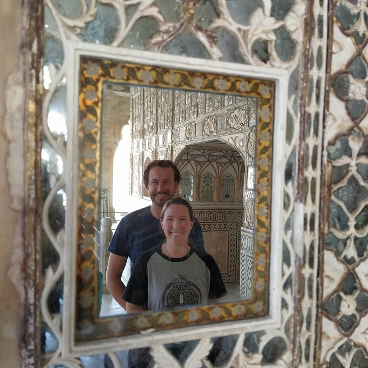 Reflet d'un couple souriant dans un miroir décoré avec des motifs muraux complexes.