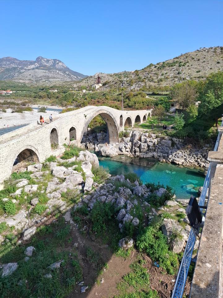 Pont de pierre au-dessus d'une rivière avec un arrière-plan montagneux.
