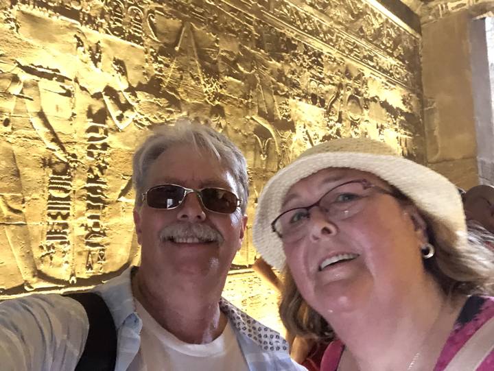 Deux personnes posant avec des sculptures anciennes en arrière-plan.