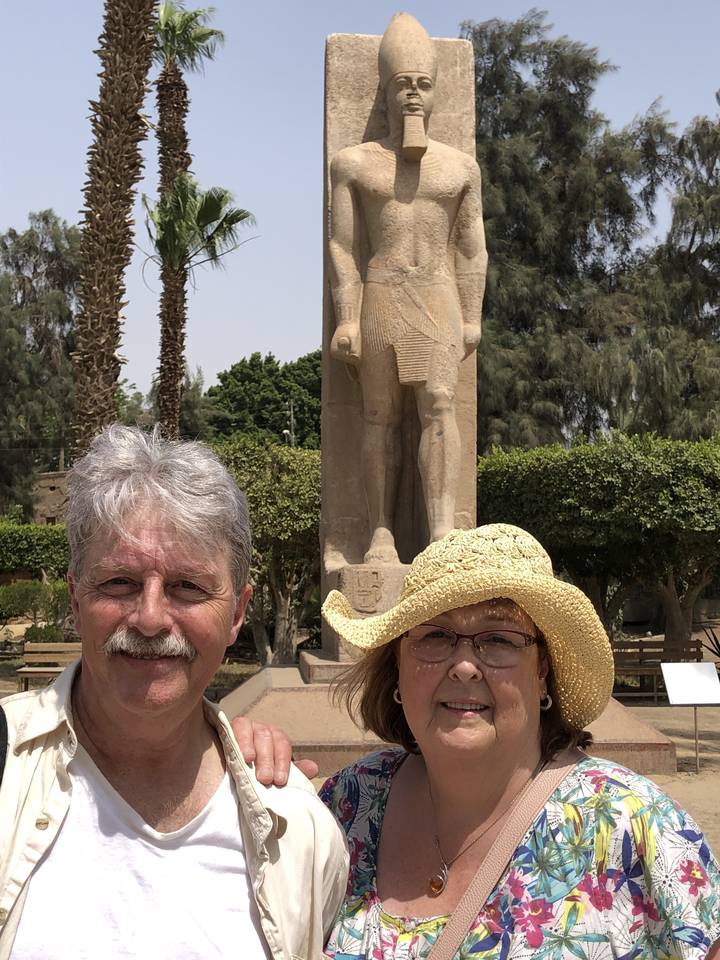 Deux personnes posant avec une statue et des palmiers.
