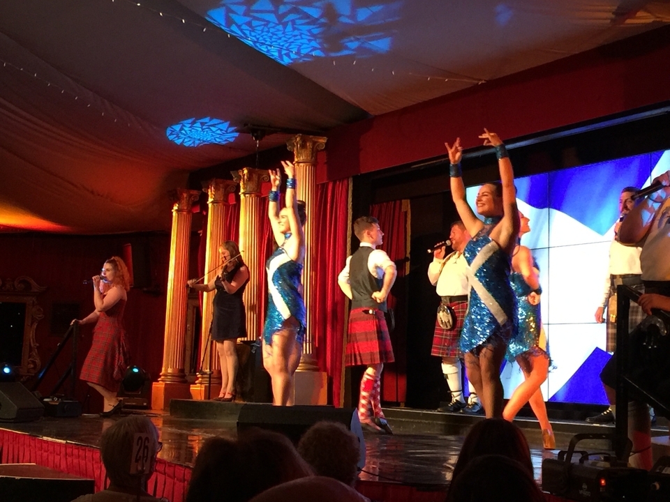 Un groupe d'artistes en tenue écossaise traditionnelle sur scène.