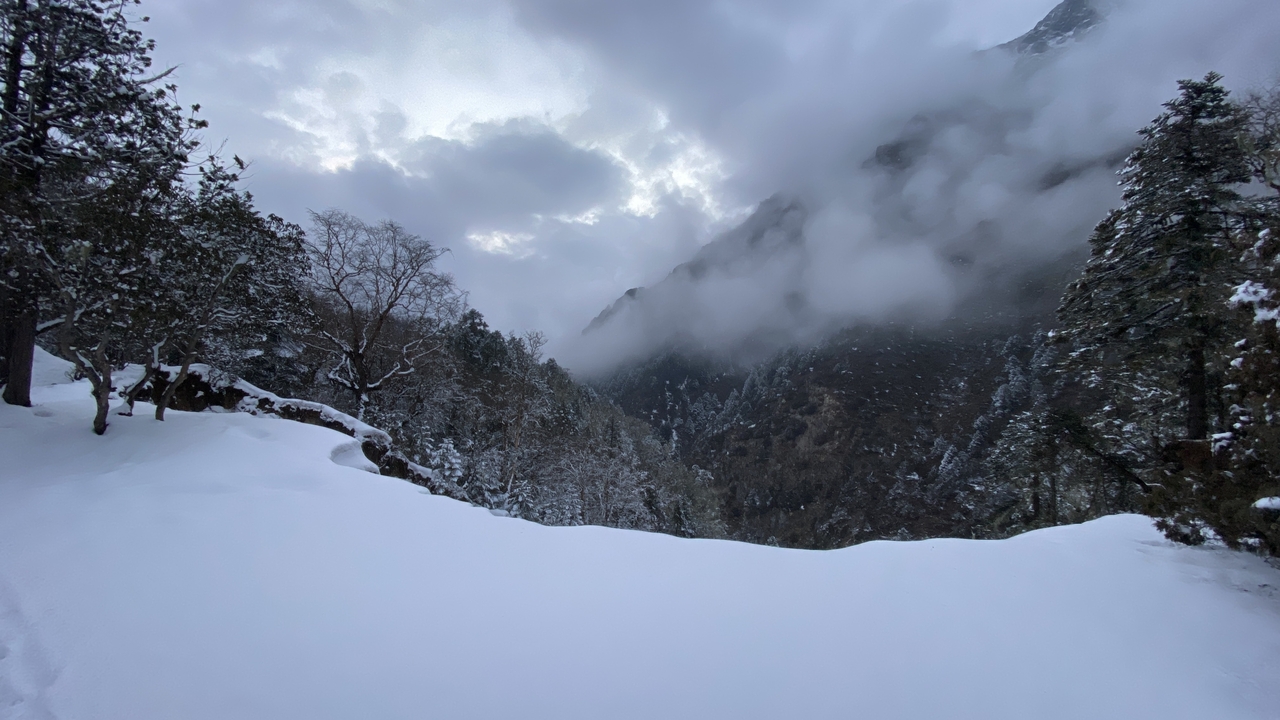 Un sentier enneigé à travers un paysage montagneux avec des nuages denses.