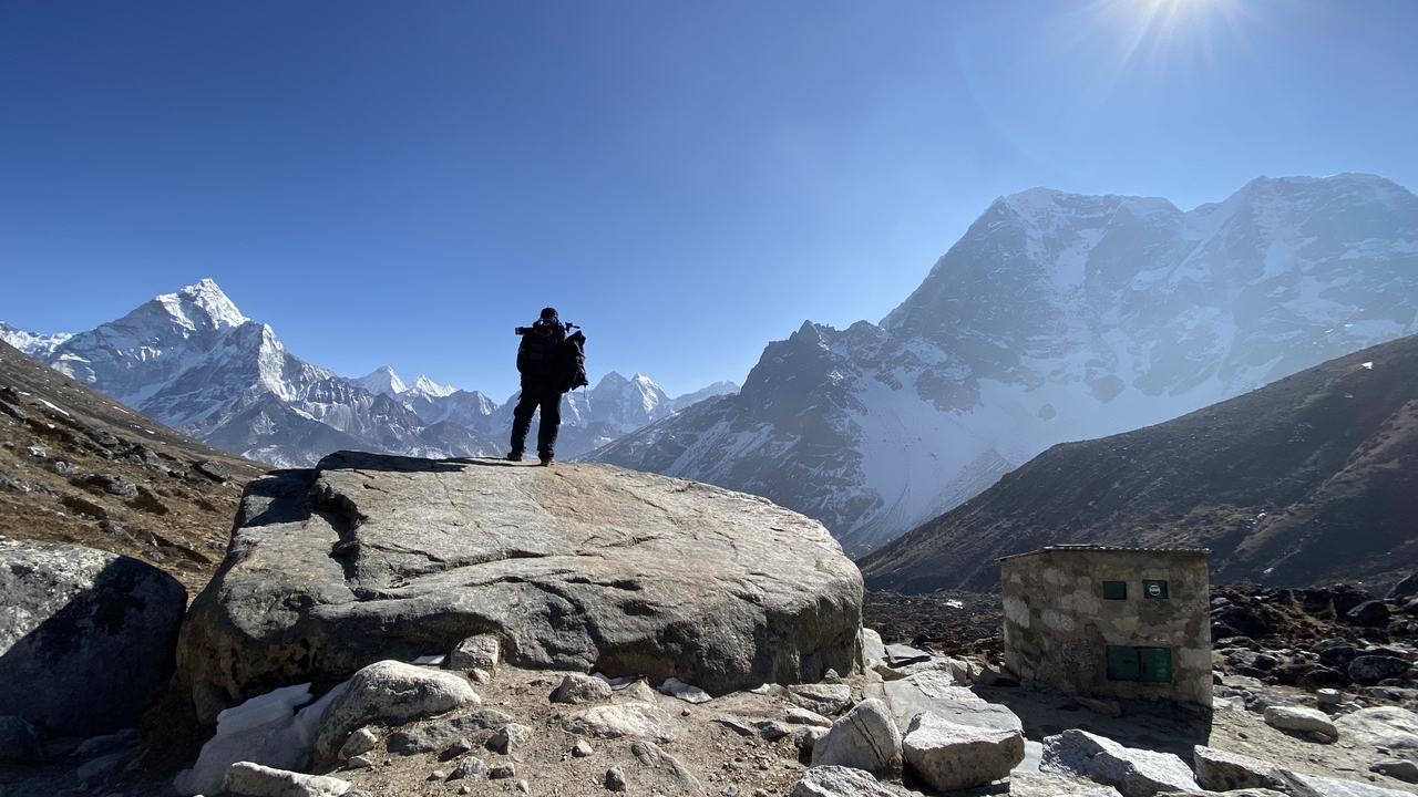 Une personne debout sur un rocher avec des montagnes enneigées en arrière-plan.