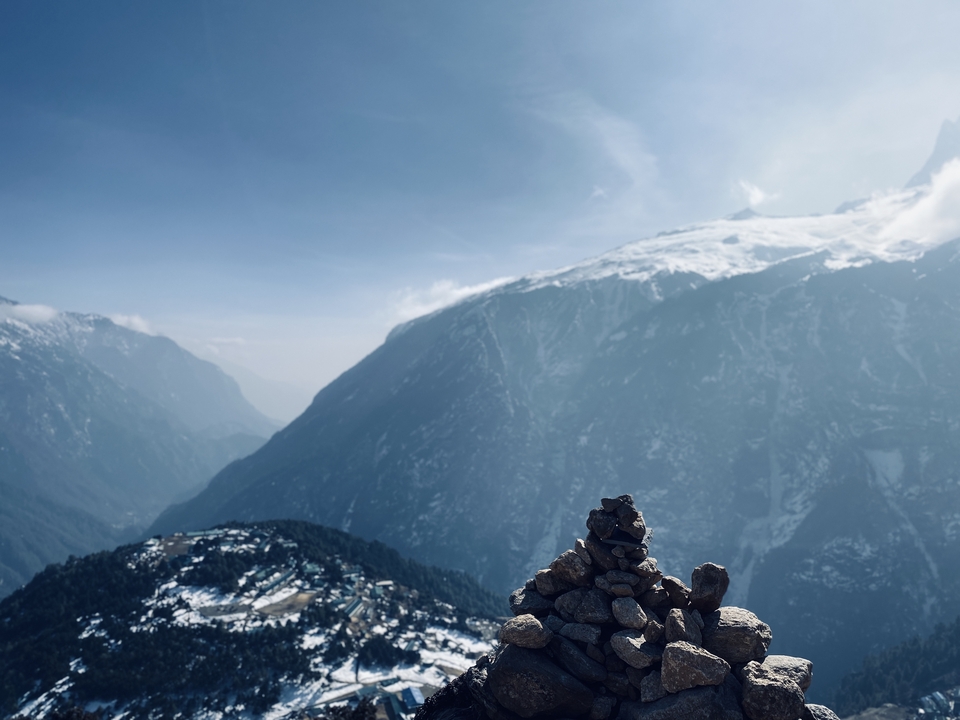Chaîne de montagnes avec des sommets enneigés et un cairn au premier plan.