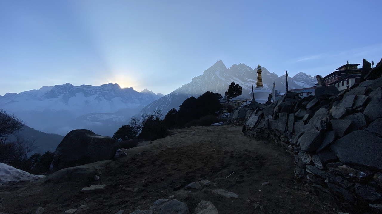 Coucher de soleil sur les montagnes avec un stupa et un mur de pierre à proximité.