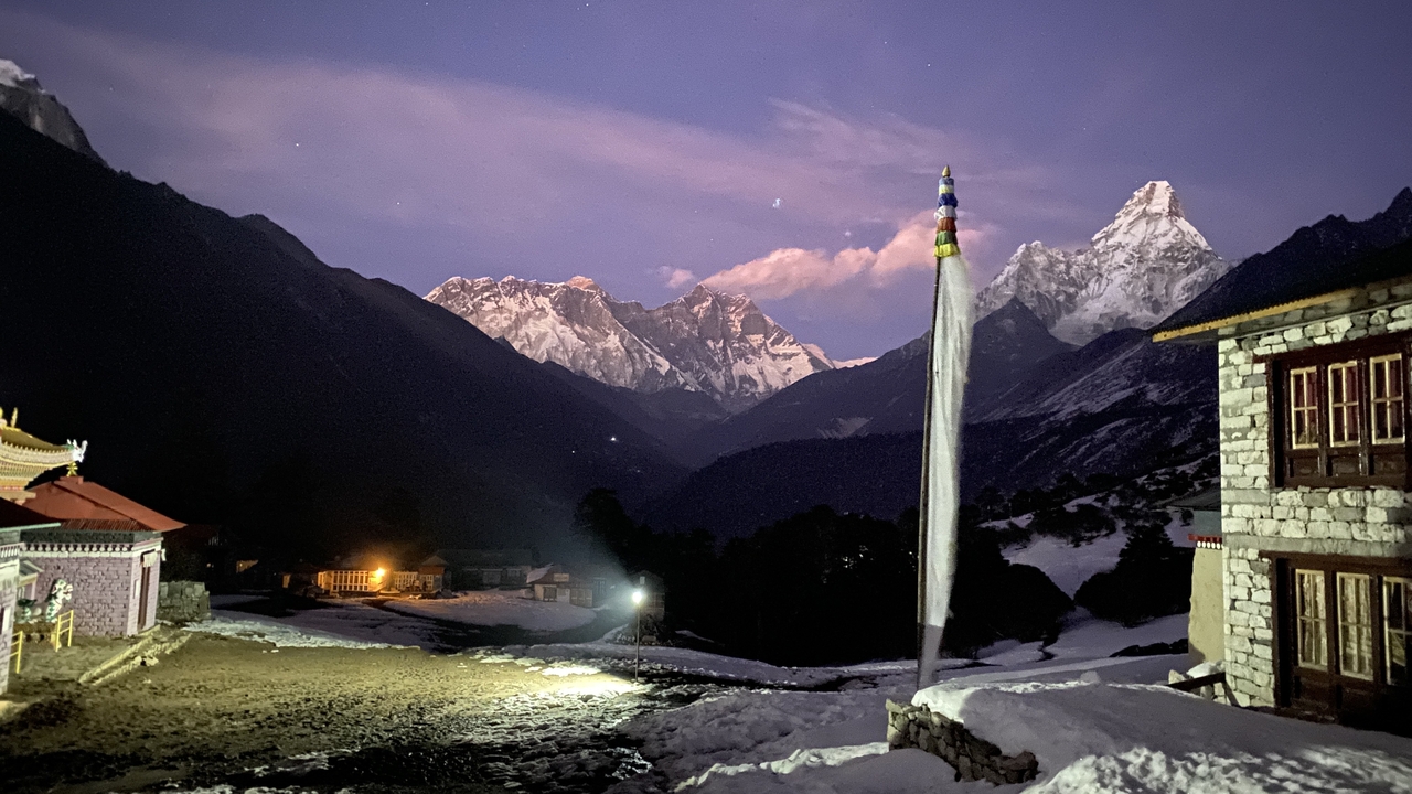 Vue nocturne de montagnes enneigées et de bâtiments avec des drapeaux de prières.
