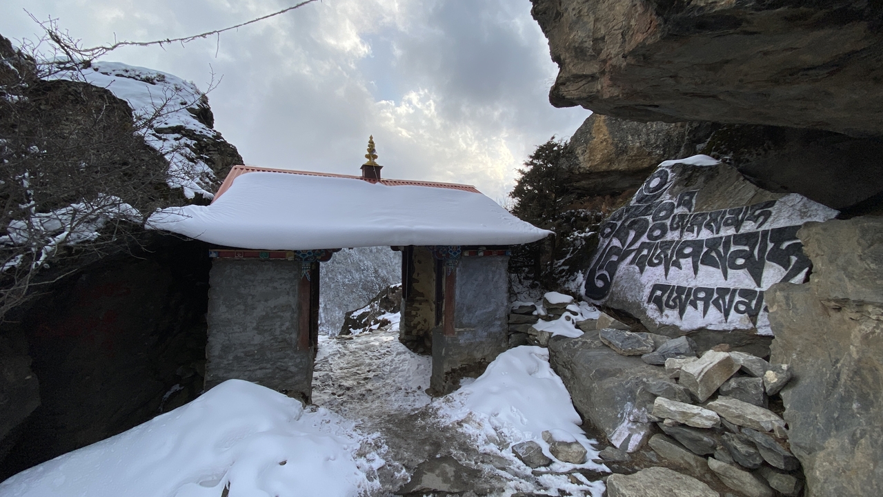 Une maison à moulin à prières encadrée par la neige et des paysages rocheux.
