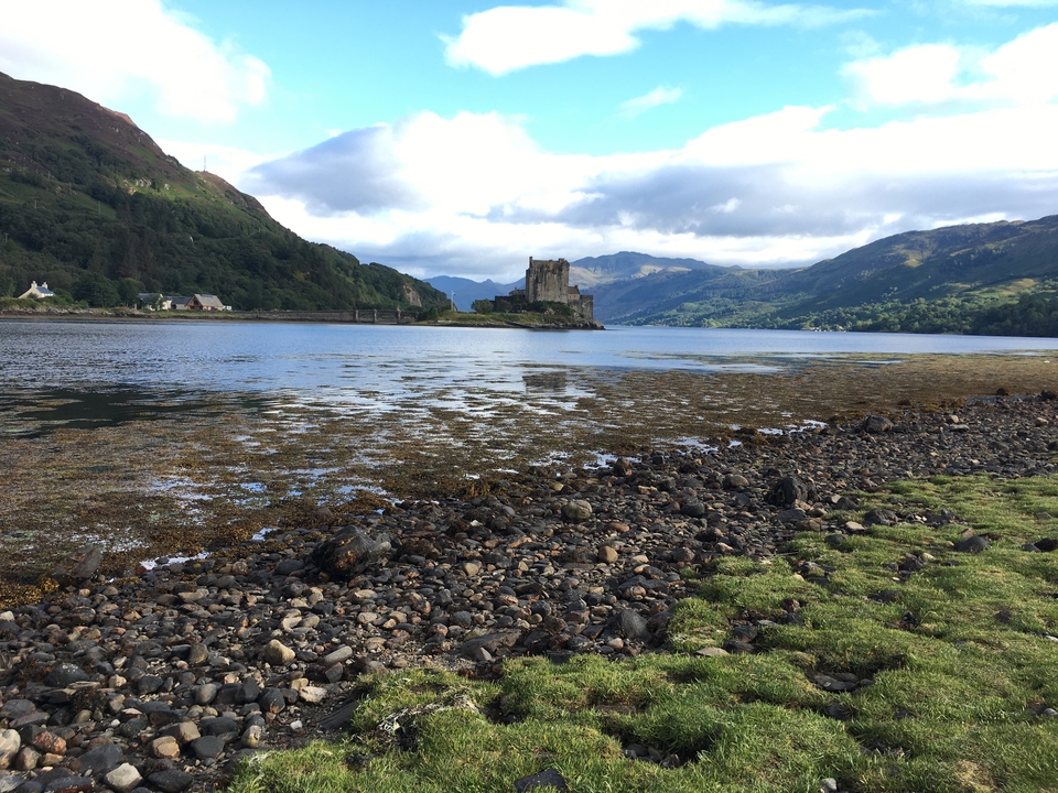 Un château au bord d'un lac avec des collines en arrière-plan.
