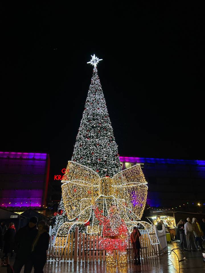 Grand sapin de Noël avec des lumières vives et un nœud géant la nuit.