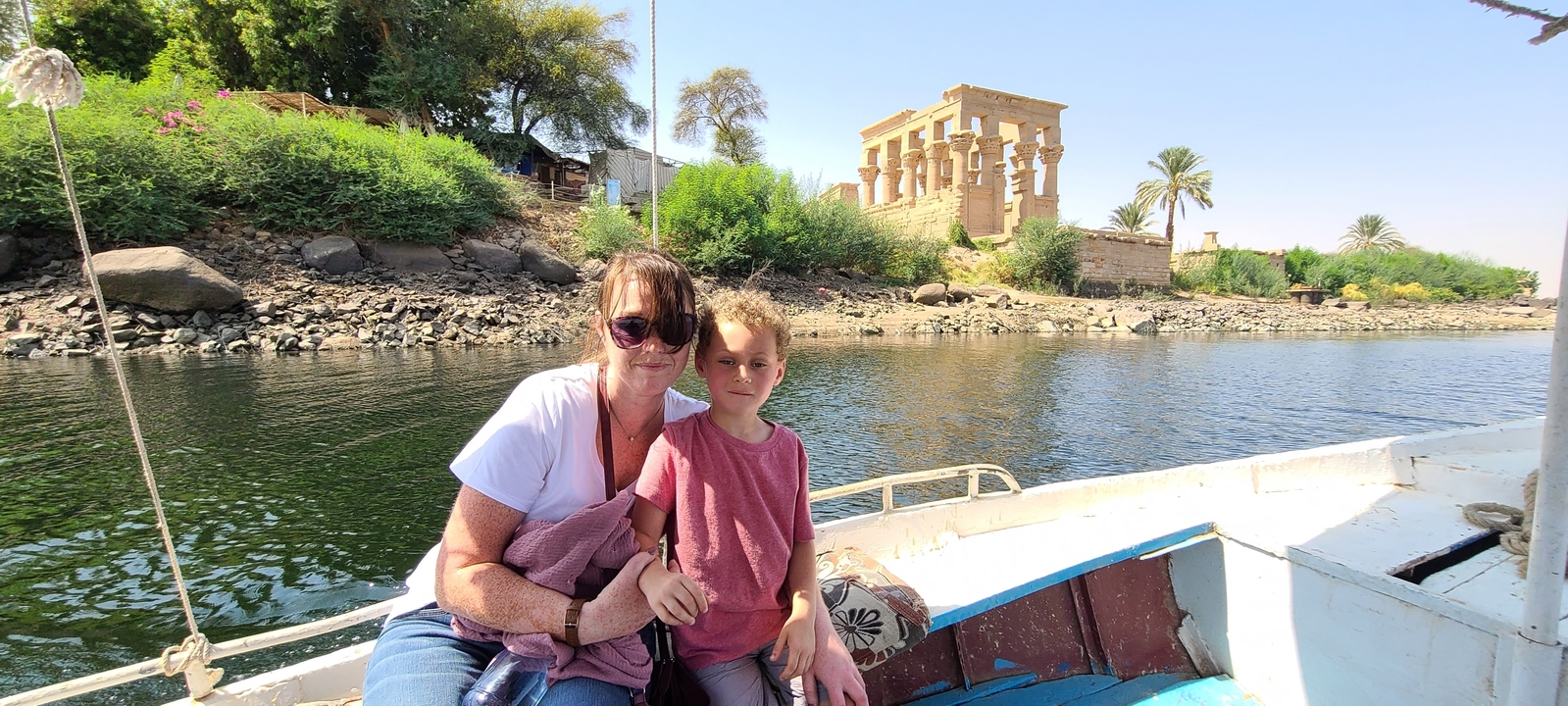 Two people on a boat with the Philae Temple in the background.