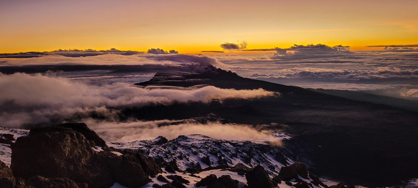 Une vue à couper le souffle d'une montagne se découpant en silhouette contre un coucher de soleil avec des nuages en contrebas.