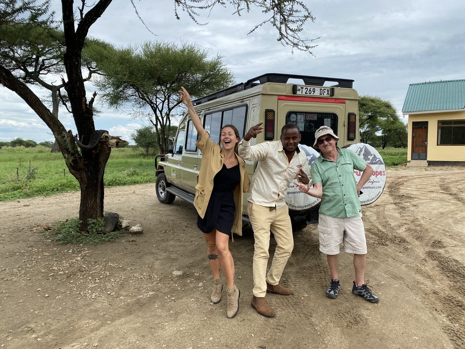 Guide and tourists celebrate beside safari vehicle under acacia tree
