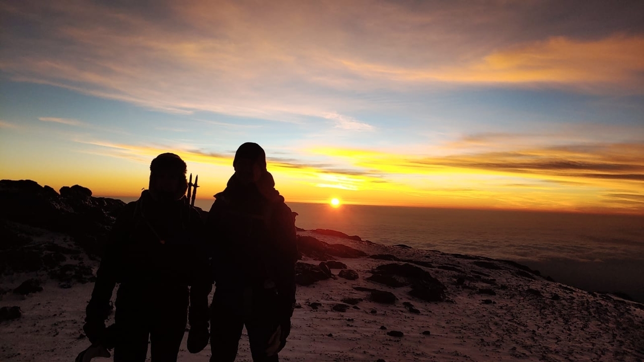 Deux personnes en silhouette contre un coucher de soleil sur une montagne enneigée.
