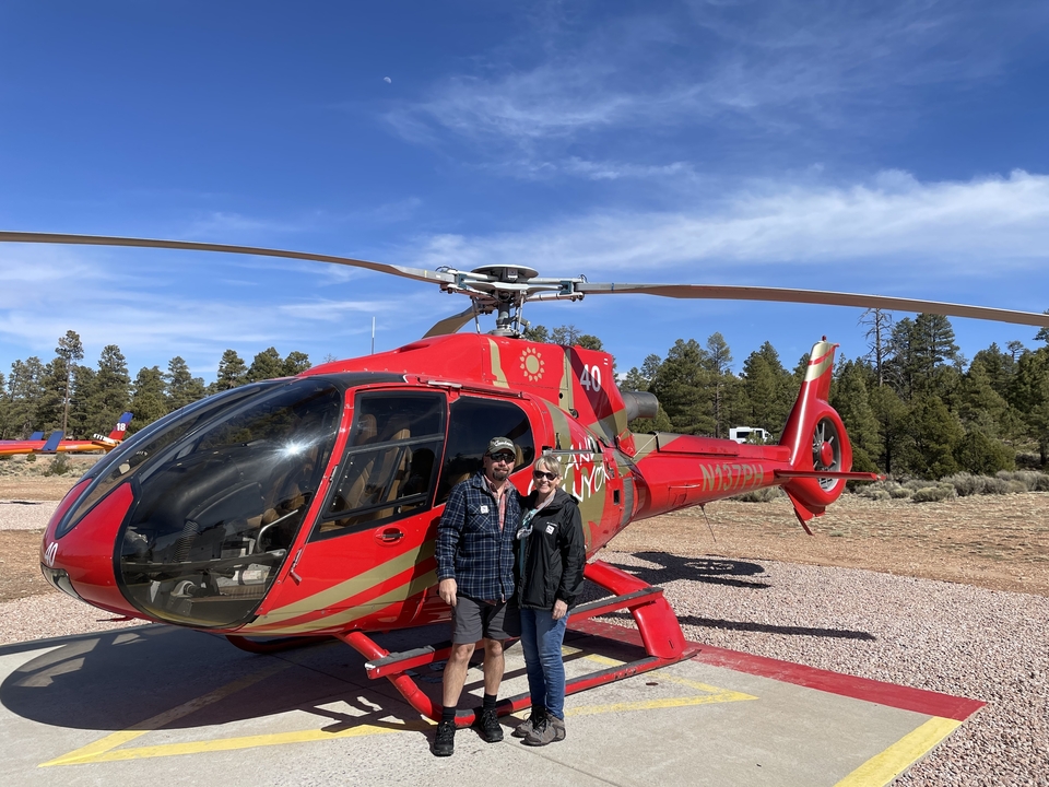 Deux personnes debout devant un hélicoptère rouge par une journée ensoleillée.