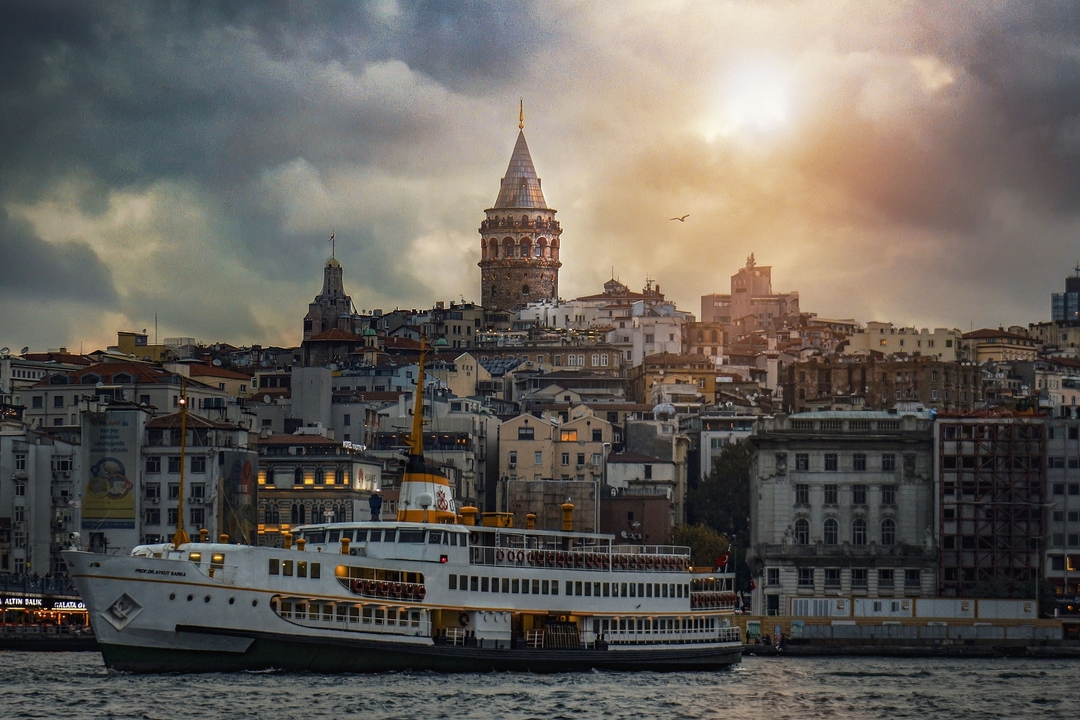 Cityscape with a boat and the Galata Tower under a golden sky.