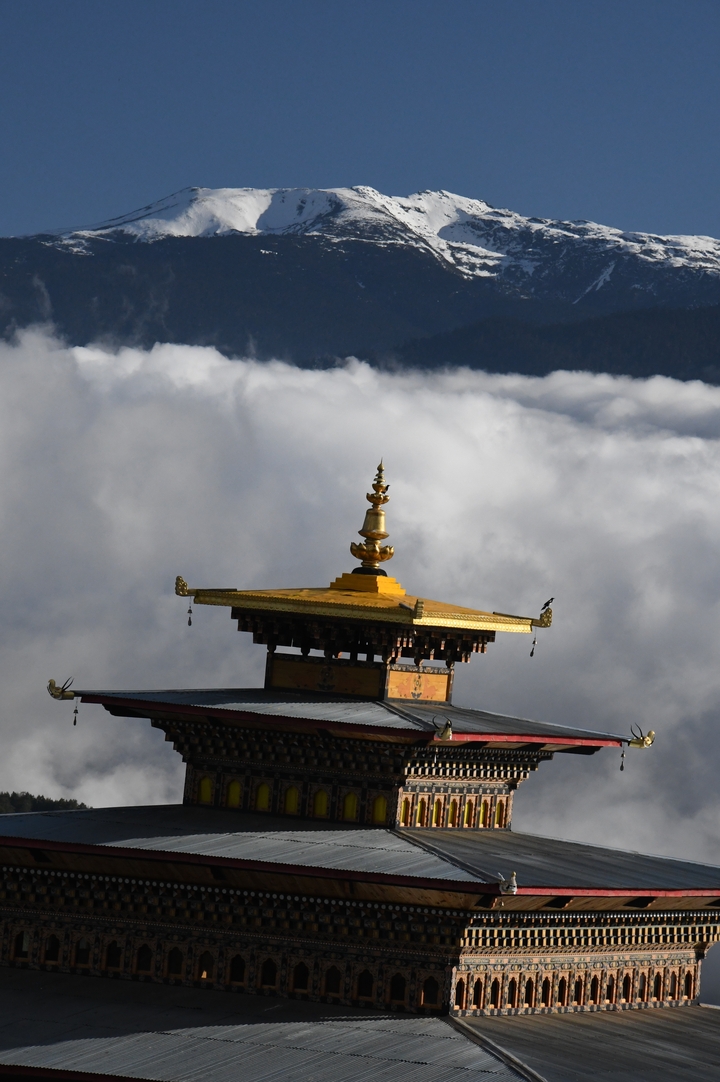 Golden temple finial rises above a sea of clouds with distant mountain ridges faintly visible.