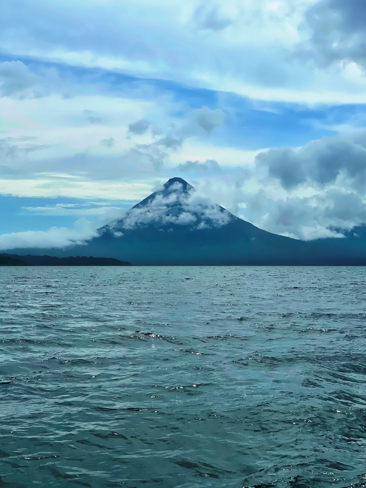 Volcan imposant couvert de nuages près d'un plan d'eau.