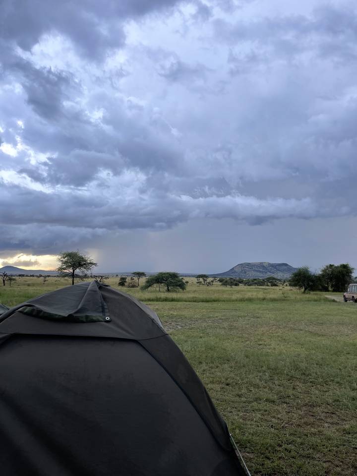 Tente de camping sur une plaine herbeuse sous un ciel nuageux.