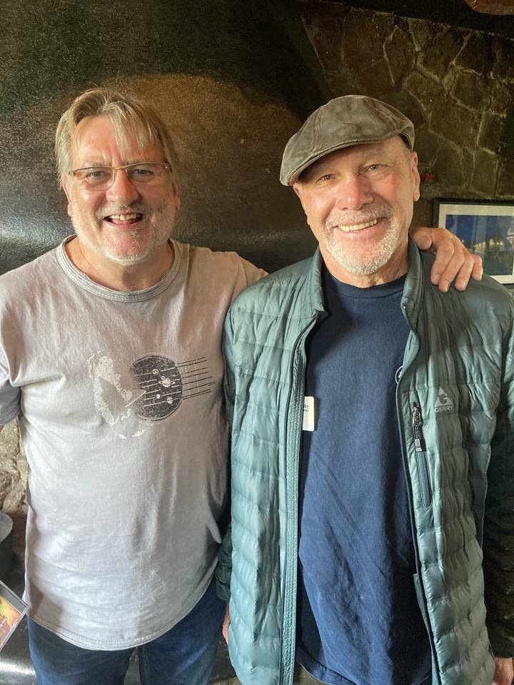 Deux hommes souriants dans un cadre rustique.