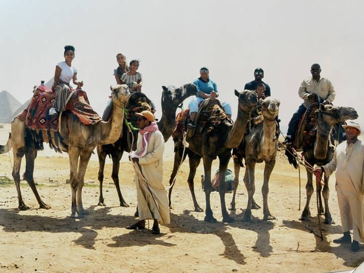 Grupo en camellos con pirámides de fondo.
