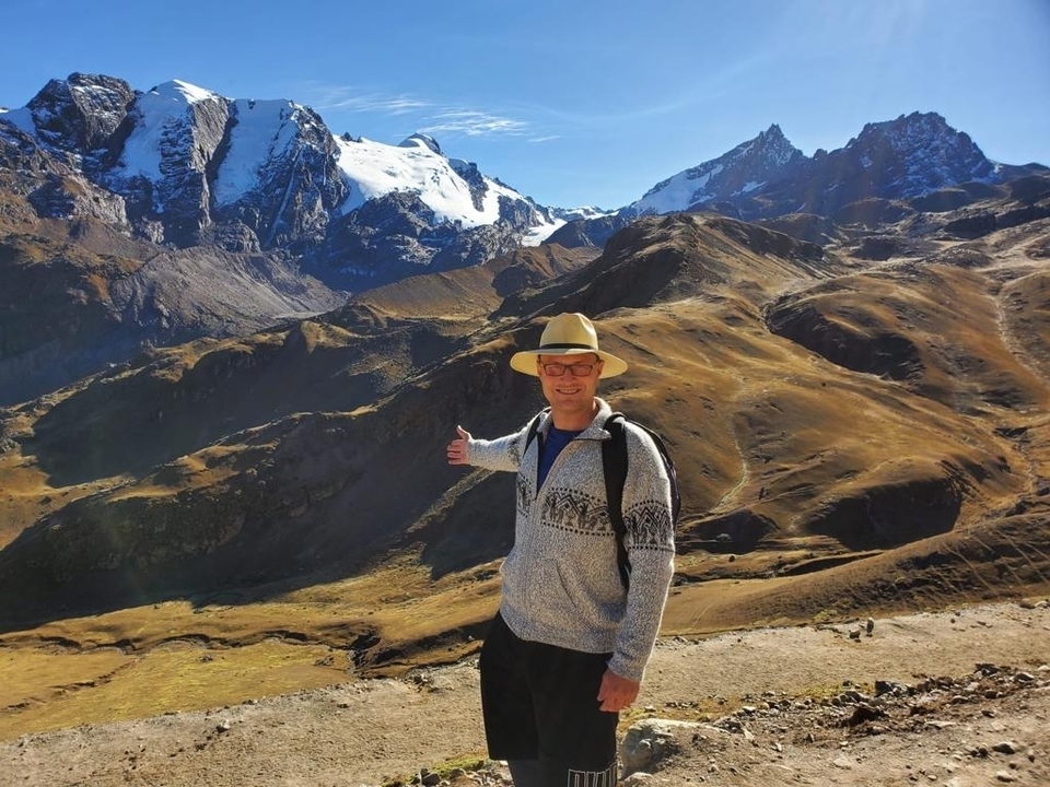 Homme posant avec d'imposantes montagnes enneigées.