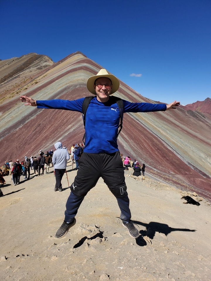 Touriste posant au Rainbow Mountain avec des collines rayées colorées.
