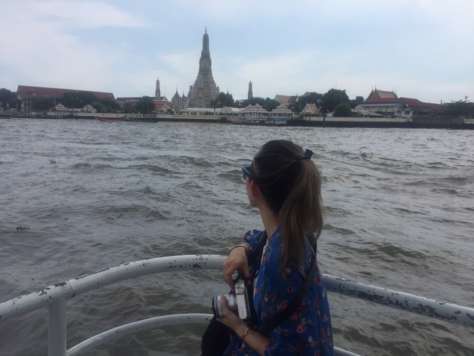 Personne sur un bateau avec vue sur un temple de l'autre côté de la rivière.