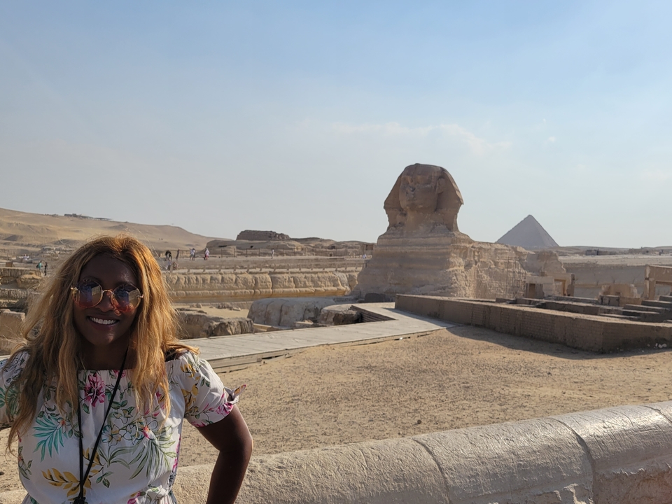 Personne debout devant le Sphinx avec une pyramide au loin.