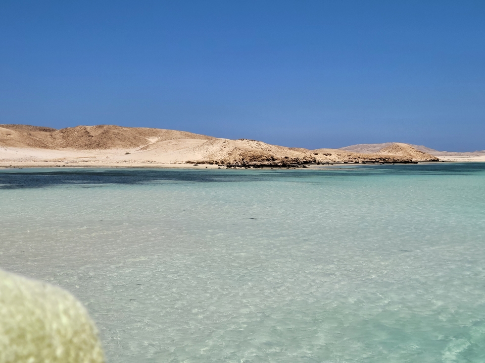 Eau turquoise calme près d'un littoral sablonneux.
