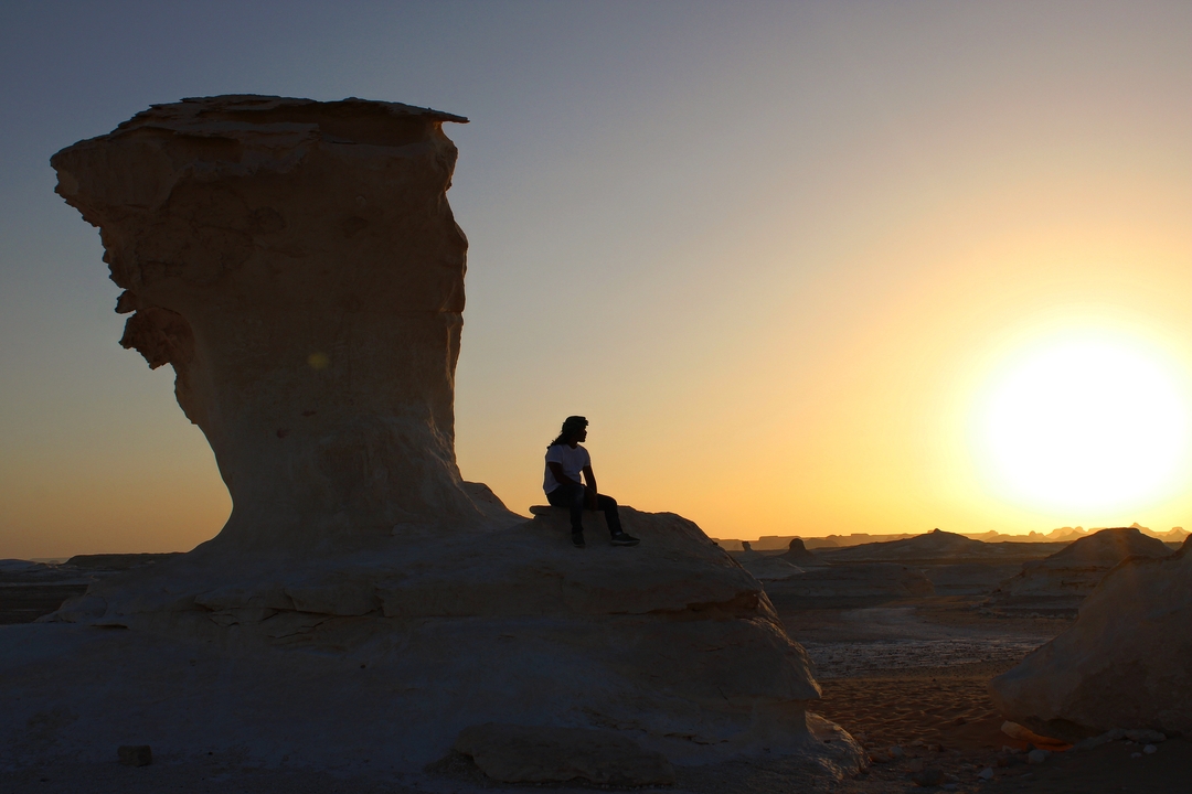 Personne assise sur des formations rocheuses au coucher du soleil.