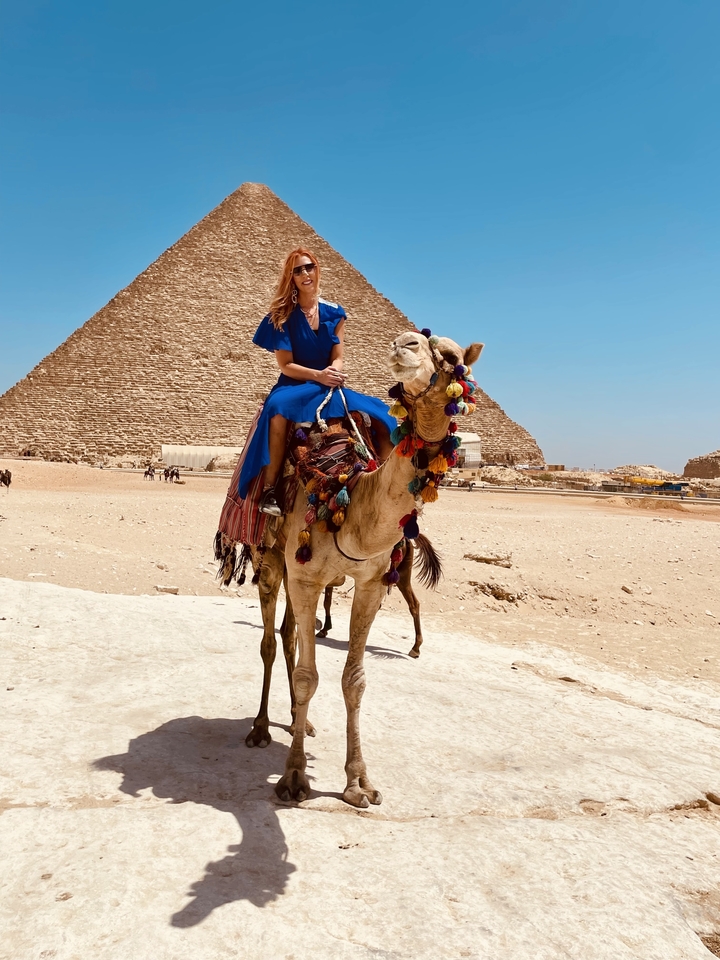 Personne montant un chameau devant des pyramides.