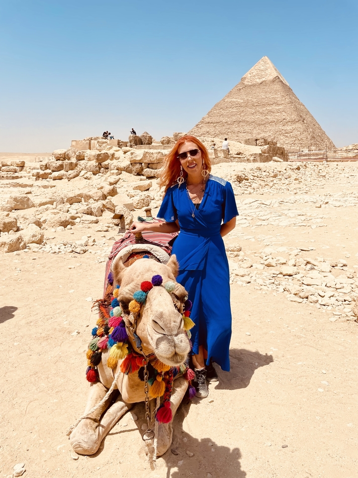 Personne debout avec un chameau devant des ruines antiques.