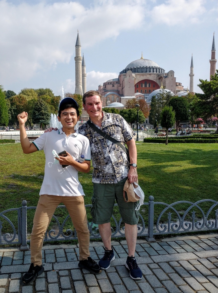 Touristes posant dans un parc avec des bâtiments historiques en arrière-plan.