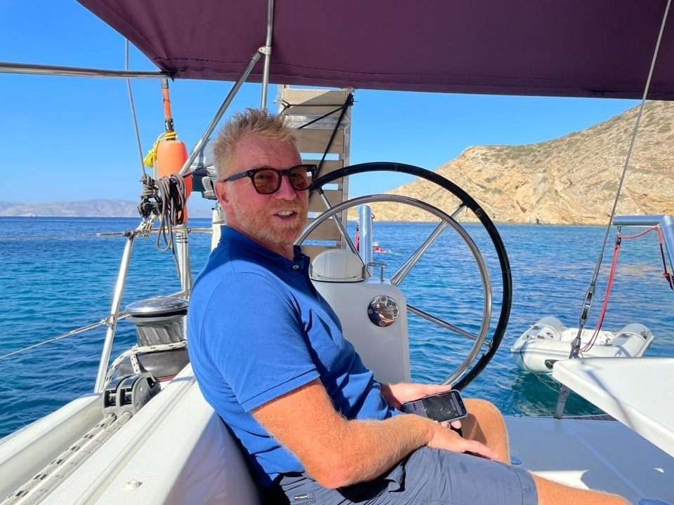 Personne à la barre d'un voilier avec un rivage rocheux.