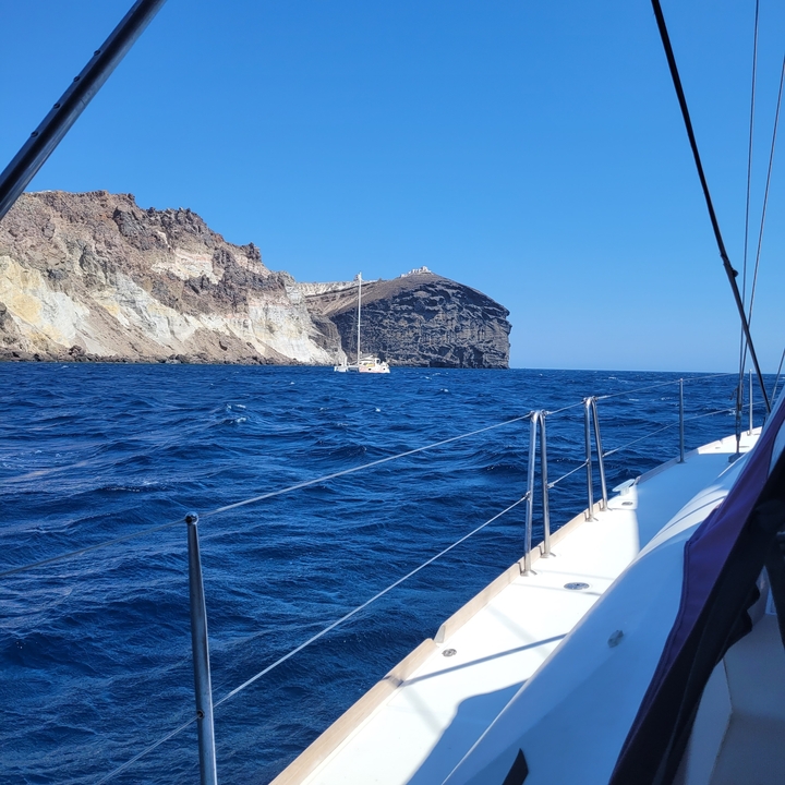 Voilier sur une mer agitée avec une côte rocheuse.