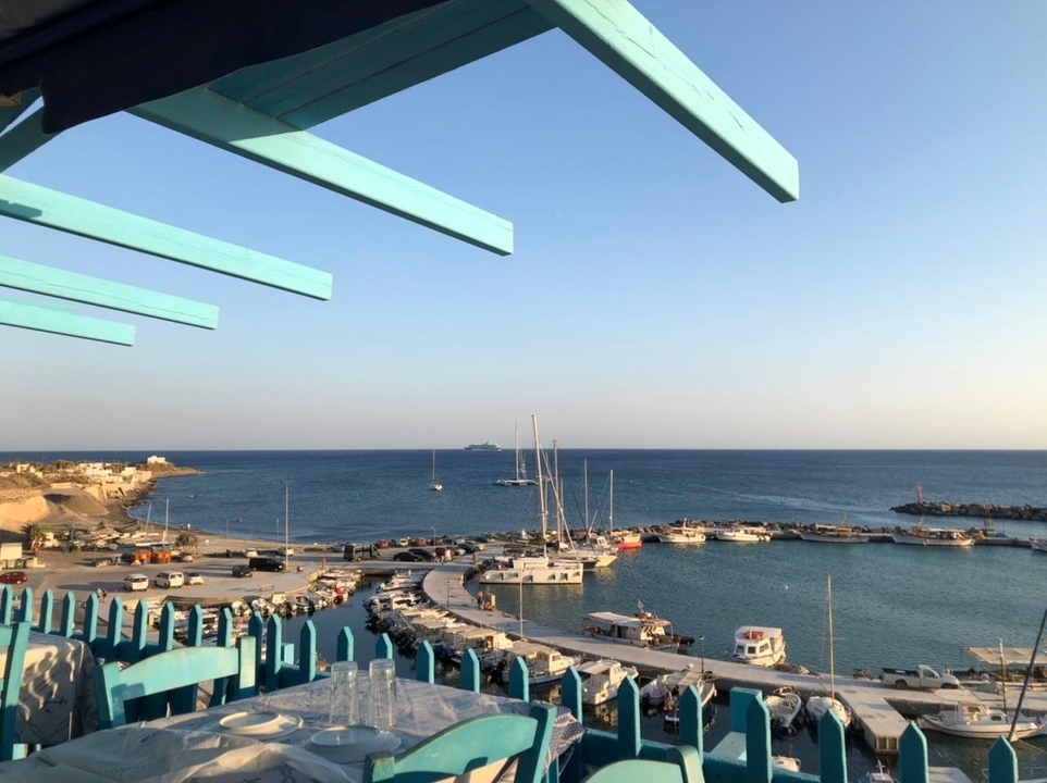 Vue d'un port de plaisance et de l'océan avec un navire de croisière au loin.