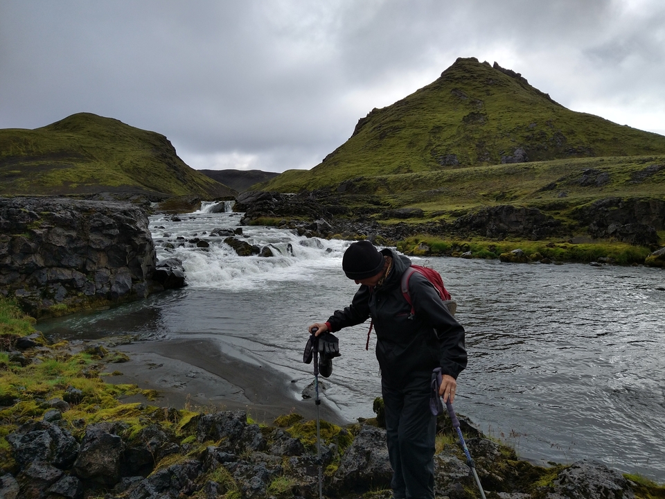 Personne marchant au bord d'une rivière dans un paysage montagneux en Islande.