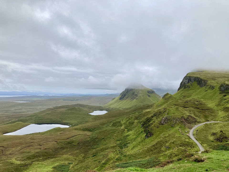 Collines verdoyantes vallonnées avec de petits lacs sous un ciel nuageux.
