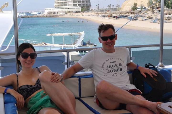 Una pareja relajándose en un barco con una playa de fondo.