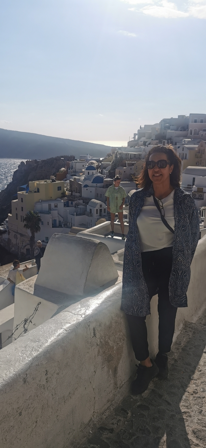Tourist smiles with the iconic white houses of Santorini cascading down the cliff behind her.