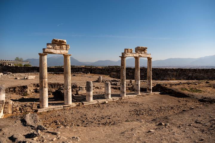 Ancient ruins with columns against a mountainous backdrop.