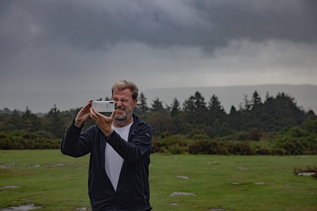Homme utilisant un appareil photo dans un paysage rural avec des nuages couverts.